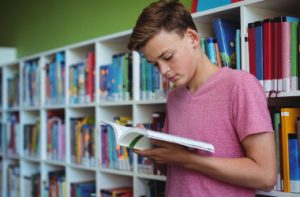 attentive-schoolboy-reading-book-library_i