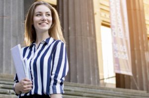 pretty-student-standing-near-university-holding-papers-her-hands-smiling-college-she-goes-school-001_i